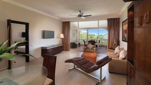Une chambre d’hôtel moderne avec une table à manger en verre, un fauteuil inclinable, un canapé, un ventilateur de plafond et une vue sur l’extérieur.