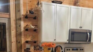 A kitchen with wooden cabinets, a microwave, a stove, a sink, and a bar area with stools. - Brand New Luxury Cabin 5 minutes to TIEC
 (Tryon)