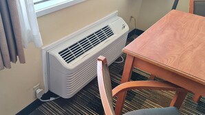 A room with a white wall-mounted air conditioner, a wooden table, and a chair.