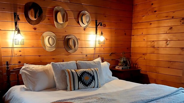 A wooden cabin-style bedroom with a bed, pillows, a blanket, and wall-mounted hats. - Panoramic View, Catskill Mountain Agri-Cabin (Gilboa)