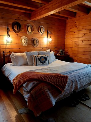 A wooden cabin-style bedroom with a bed, pillows, a blanket, and wall-mounted hats.