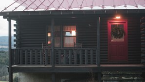 A log cabin with a porch, a red door, and a wreath on the door. - Panoramic View, Catskill Mountain Agri-Cabin (Gilboa)