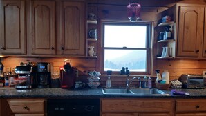 A kitchen with wooden cabinets, a coffee maker, a kettle, a sink, and a window with a view of trees. - Panoramic View, Catskill Mountain Agri-Cabin (Gilboa)