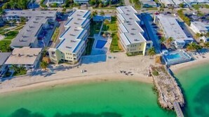 An aerial view of a coastal hotel with multiple buildings, a sandy beach, and a clear turquoise sea. - Ocean Oasis!OceanView-Beach/Pool (Key Colony Beach)