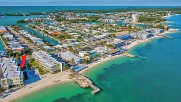 An aerial view of a coastal resort with multiple buildings, a pier, and clear turquoise waters. - Ocean Oasis!OceanView-Beach/Pool (Key Colony Beach)