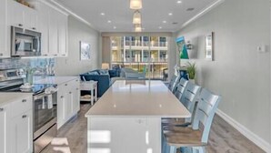 A modern kitchen with white cabinetry, a central island, and a dining area with blue chairs. - Ocean Oasis!OceanView-Beach/Pool (Key Colony Beach)