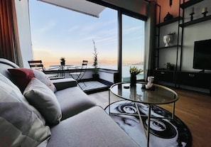 A modern living room with a sofa, a round glass coffee table, and a view of the cityscape through large windows. - Your second home w/stunning view (Istanbul)