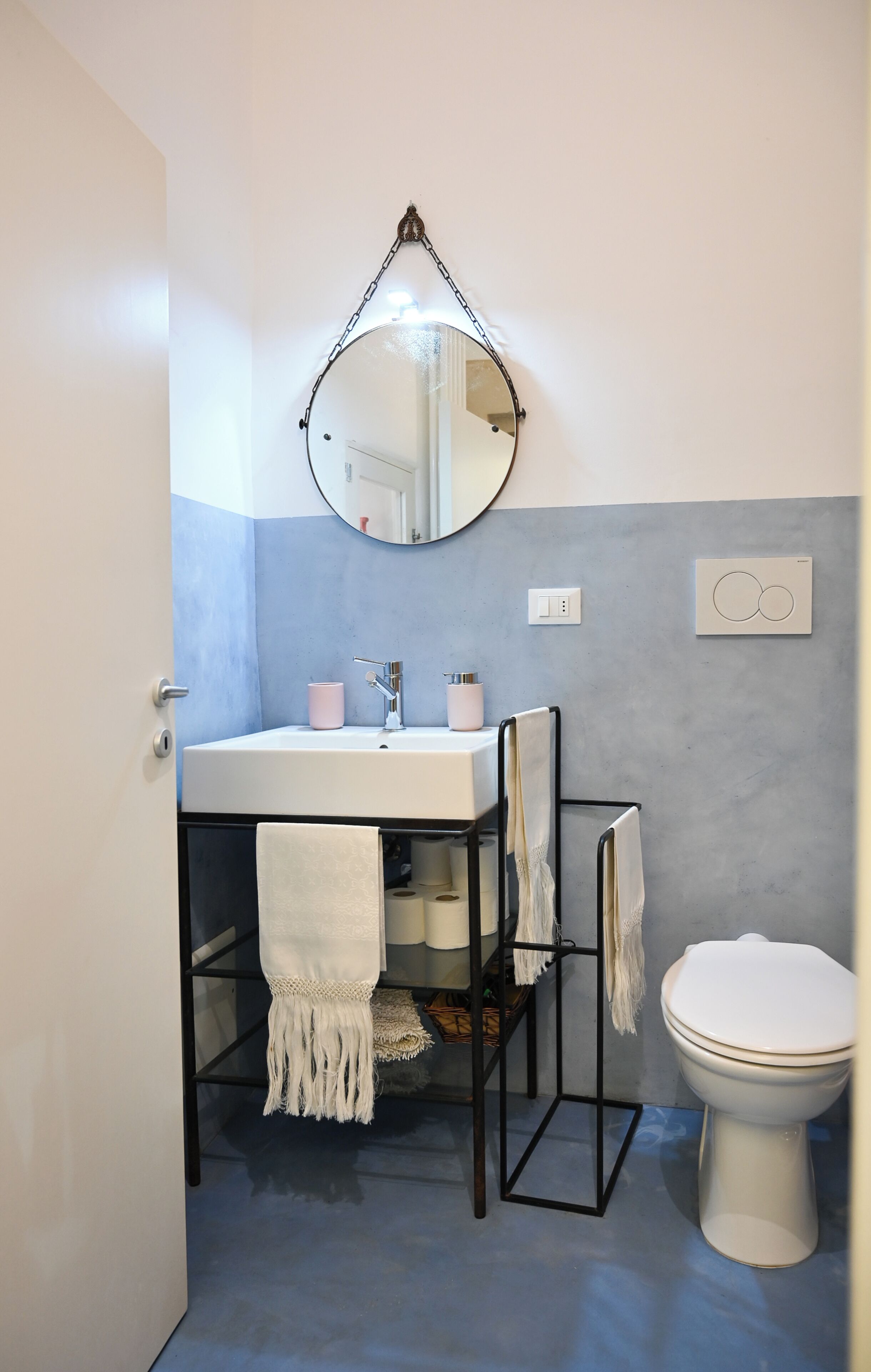 A bathroom with a white sink, a round mirror, a toilet, and towels hanging on a rack.