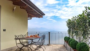 Un balcon avec une table préparée pour le petit-déjeuner, des plantes en pot et une vue sur les montagnes lointaines.