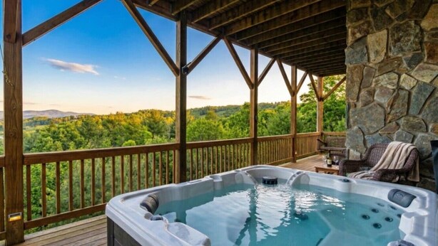 A hot tub on a wooden deck with a stone wall and a view of a forest.