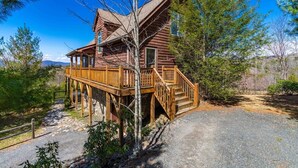 A wooden cabin with a deck, surrounded by trees and a clear sky.