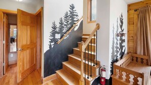 A staircase with a black and white forest mural, wooden doors, and a fire extinguisher.