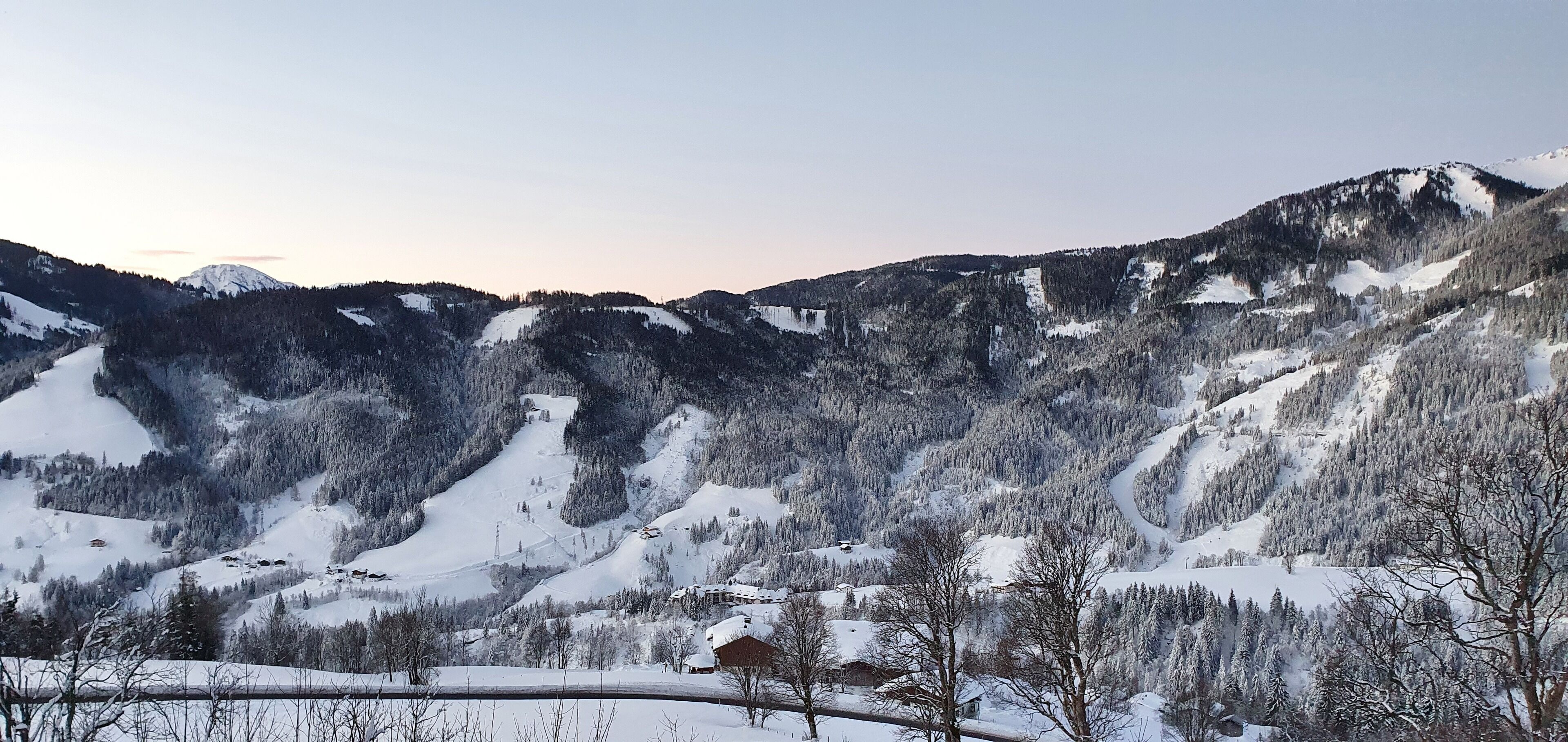 A mountainous landscape with snow-covered slopes and a few buildings nestled among the trees.