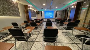 A conference room with a large screen at the front, rows of chairs, and a patterned wall. - Rue d'Or (Setif)