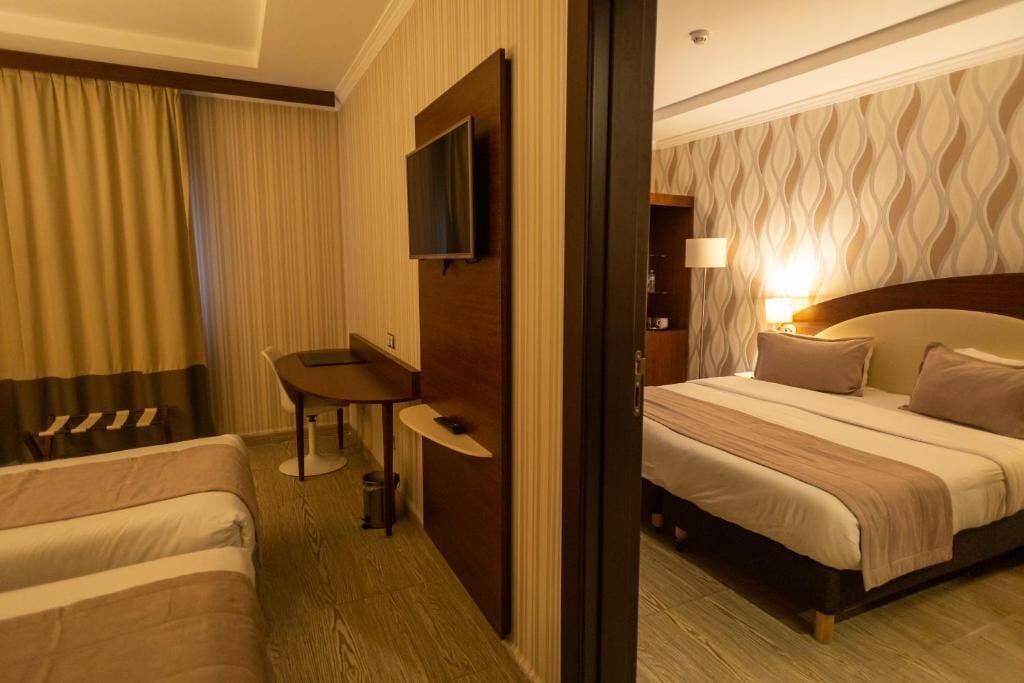 Habitación de hotel con cama, escritorio, silla, televisor y lámpara.