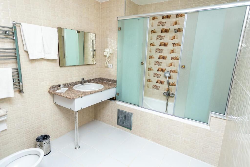 A bathroom with a sink, mirror, towel rack, and a shower with a patterned glass door.