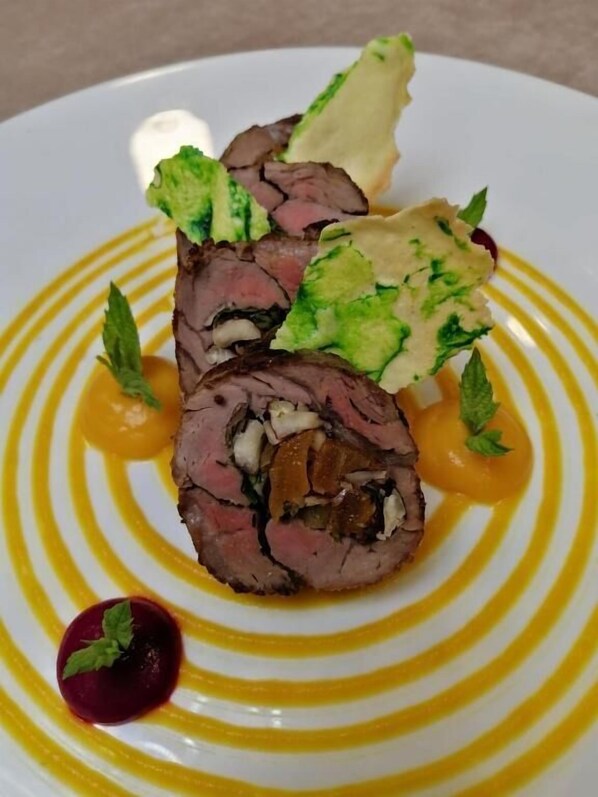A plate of food with slices of meat, avocado, and a beet garnish.