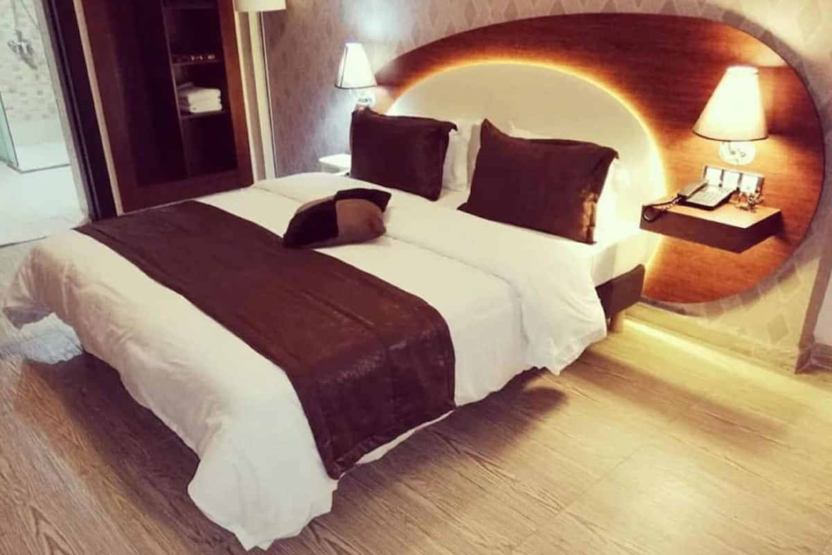 A hotel room with a bed, bedside lamps, a nightstand, and a headboard with a built-in light.