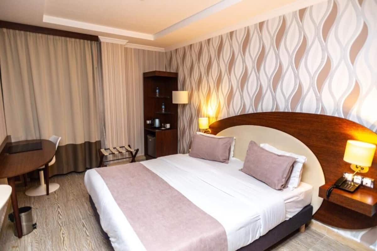 A hotel room with a large bed, a desk, a chair, a small table, and a minibar.