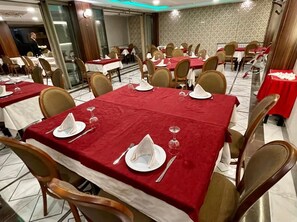 A dining area with tables set for four, each with red tablecloths, white napkins, and cutlery.