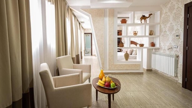 A hotel lobby with a seating area, a fruit bowl on a table, and a decorative shelf with pottery and a camel figurine. - Rue d'Or (Setif)
