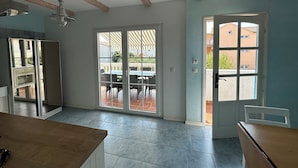 A room with a large sliding glass door leading to an outdoor patio, a kitchen area with a wooden countertop, and a ceiling with exposed wooden beams. - Apartment 3, Apartment mit Meerblick (Vodice)