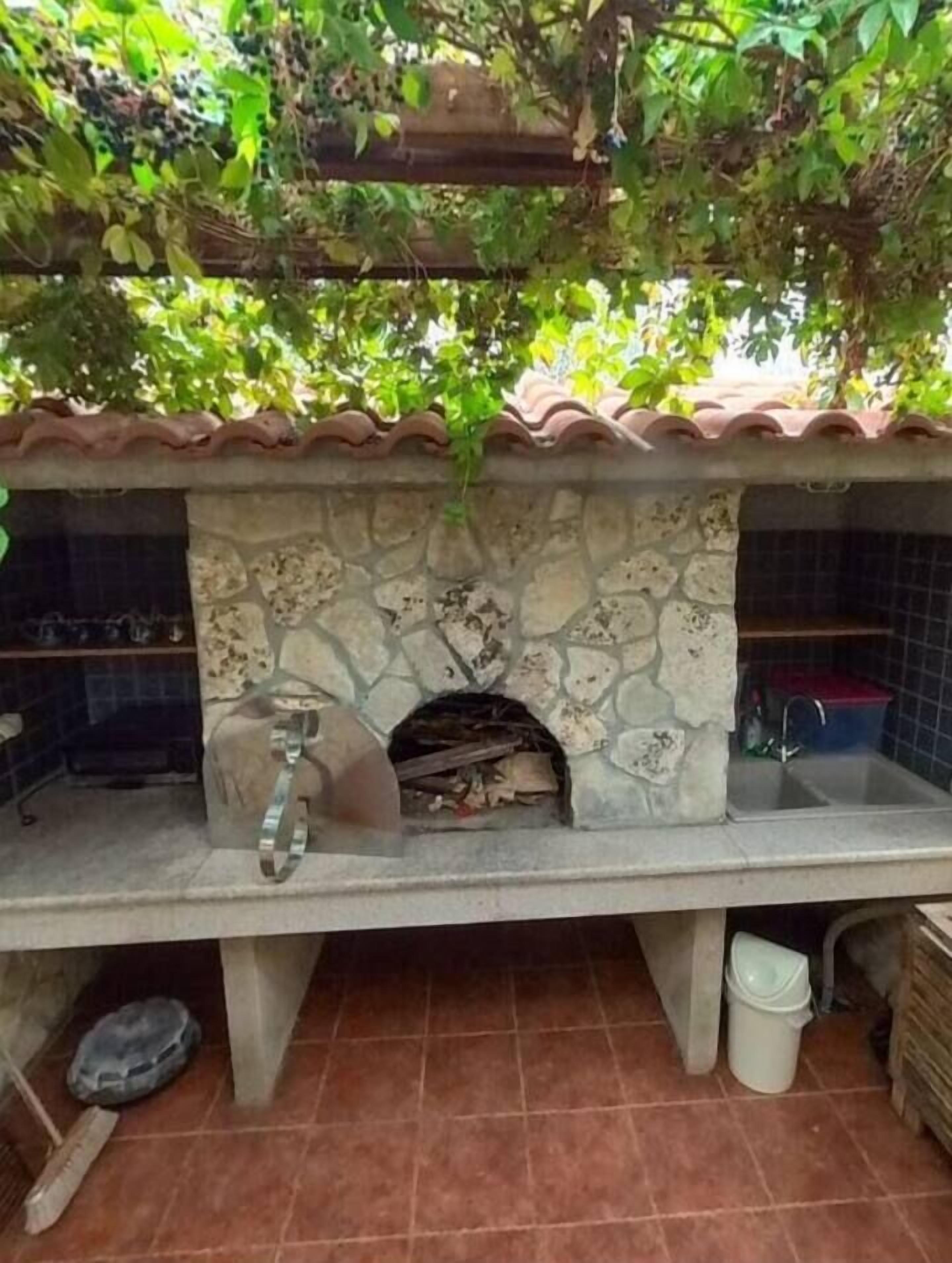 An outdoor kitchen with a stone fireplace, a sink, and a tiled floor.