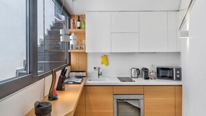 A modern kitchen with a built-in oven, microwave, and sink. There is a window with a view of a staircase.