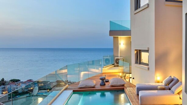 A modern pool area with a clear view of the sea, a glass balustrade, and a minimalist building structure.