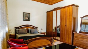 Ein Schlafzimmer mit einem hölzernen Bett, einem Schrank, einem roten Sessel und einem Tisch mit Glasplatte.