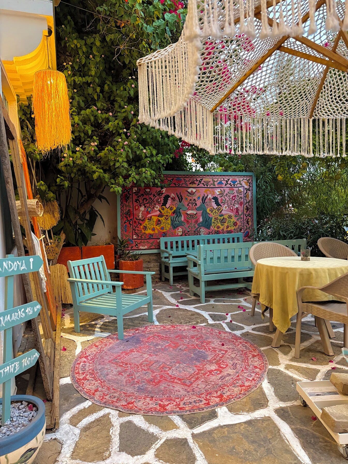 Un espacio al aire libre acogedor con mobiliario de mimbre, un tapete colorido y una lámpara colgante de macramé.