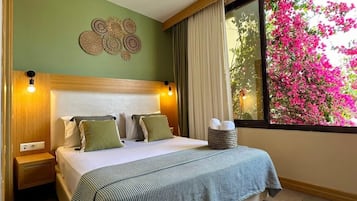 Habitación de hotel con cama, mesitas de noche, una decoración en la pared, una ventana y vistas a flores rosadas.