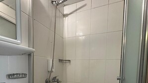 A bathroom with a white sink, a mirror, a shower with a handheld showerhead, and tiled walls. - Andoya Pension (Bodrum)