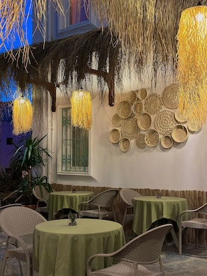 An outdoor dining area with round tables covered in green tablecloths, wicker chairs, and hanging light fixtures. - Andoya Pension (Bodrum)