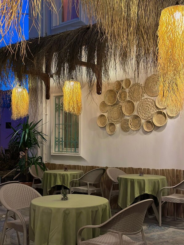 An outdoor dining area with round tables covered in green tablecloths, wicker chairs, and hanging light fixtures. - Andoya Pension (Bodrum)