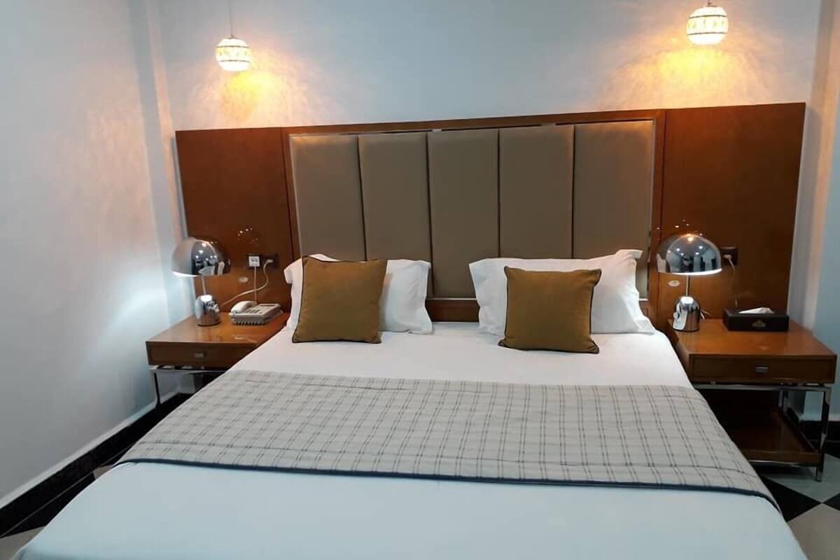 A hotel room with a large bed, two bedside tables, a headboard, and two wall-mounted lamps.