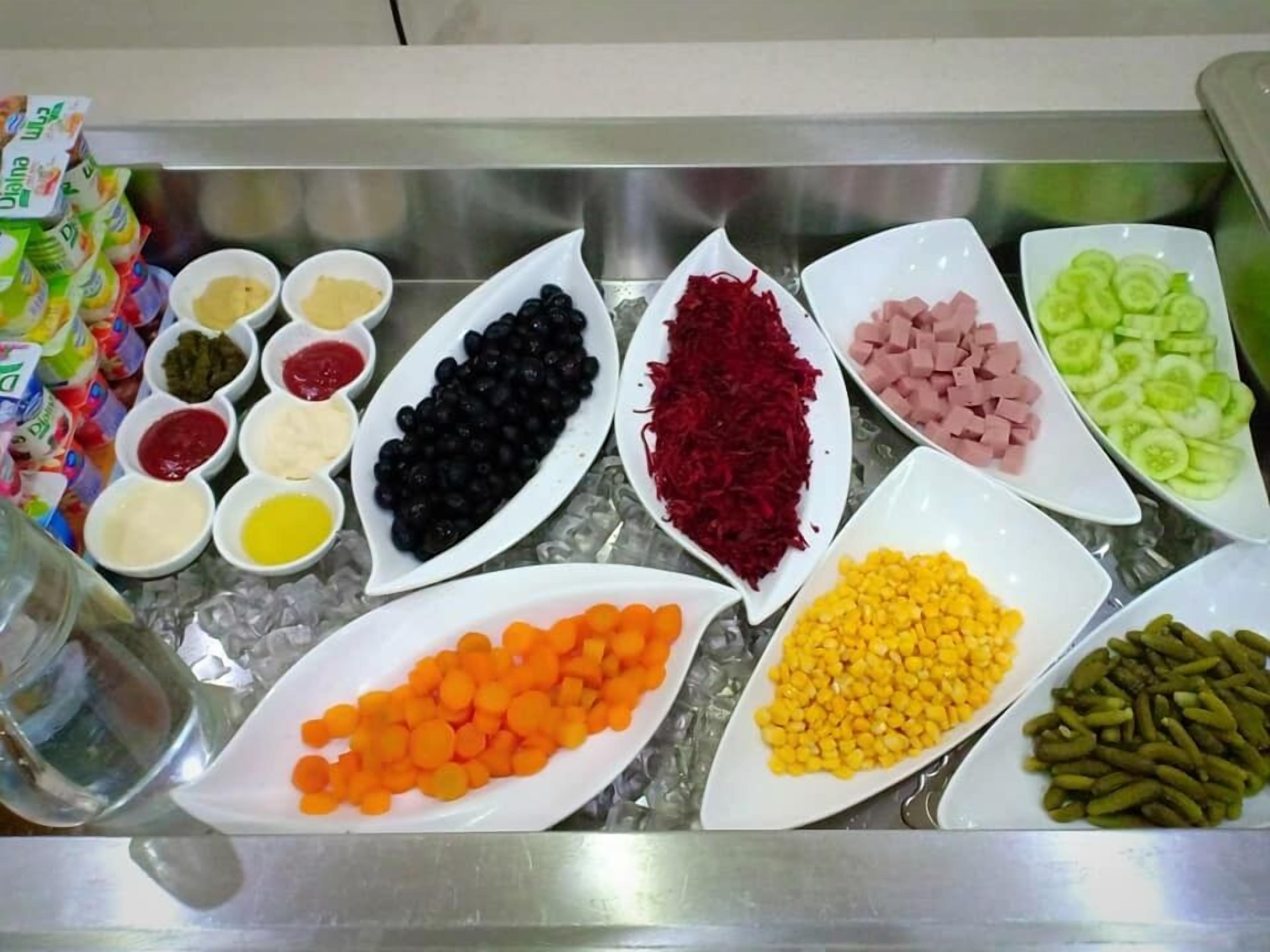 A buffet with various food items including black beans, beets, ham, cucumbers, carrots, corn, and pickles.