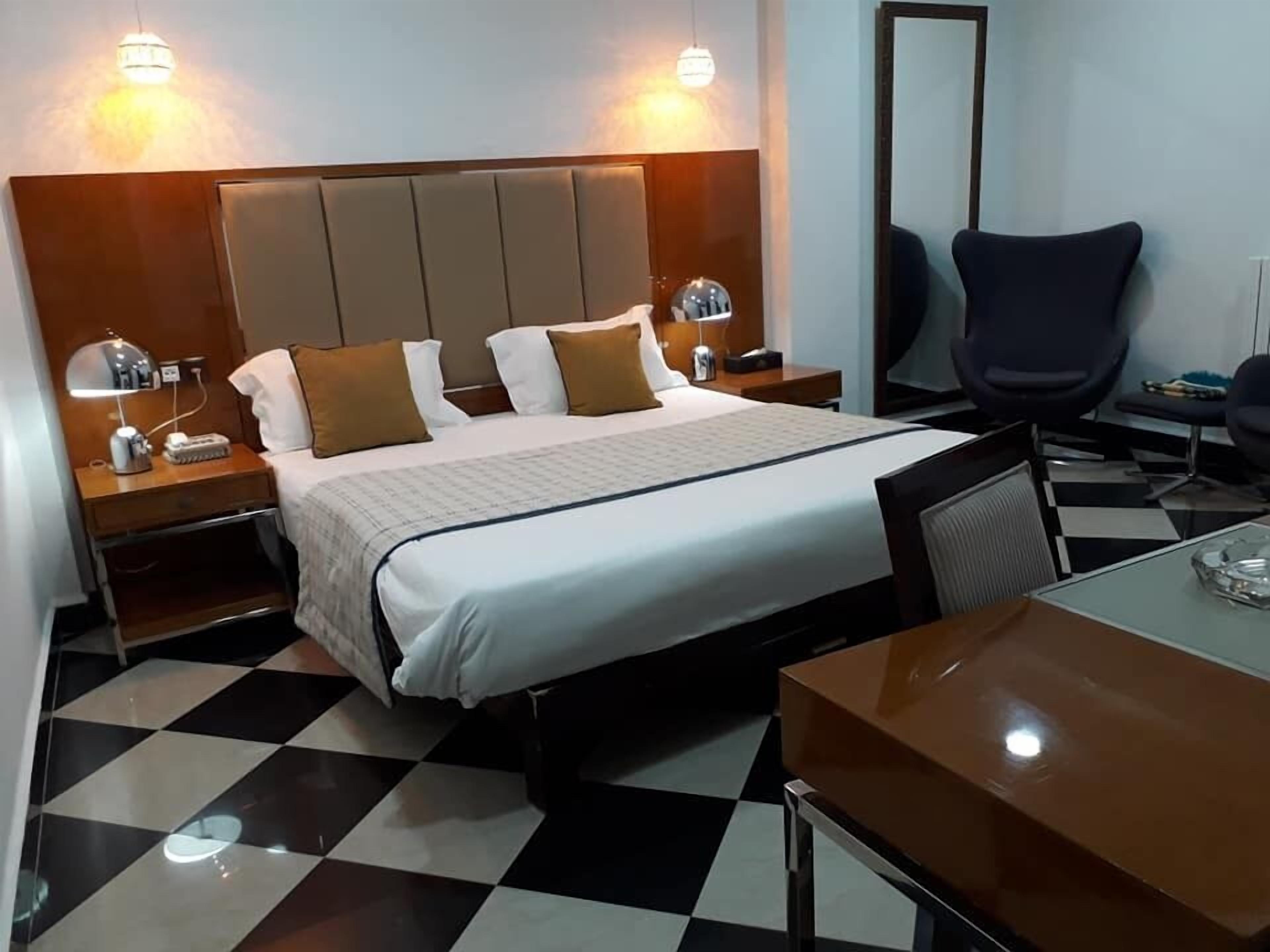 Une chambre d’hôtel avec un lit, deux tables de chevet avec des lampes, un bureau, une chaise et un grand miroir au mur.