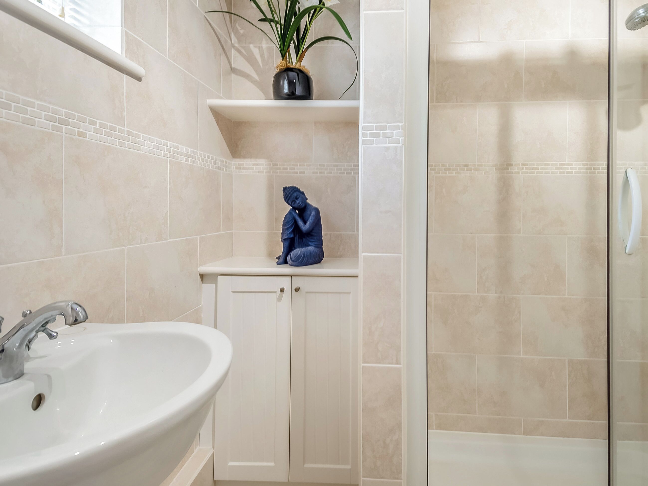 A bathroom with a white sink, a shower, and a cabinet with a blue statue.