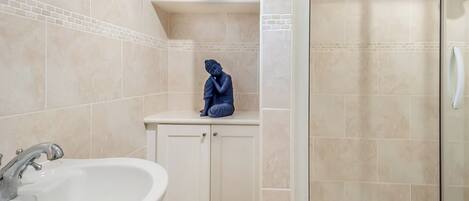 A bathroom with a white sink, a shower, and a cabinet with a blue statue.