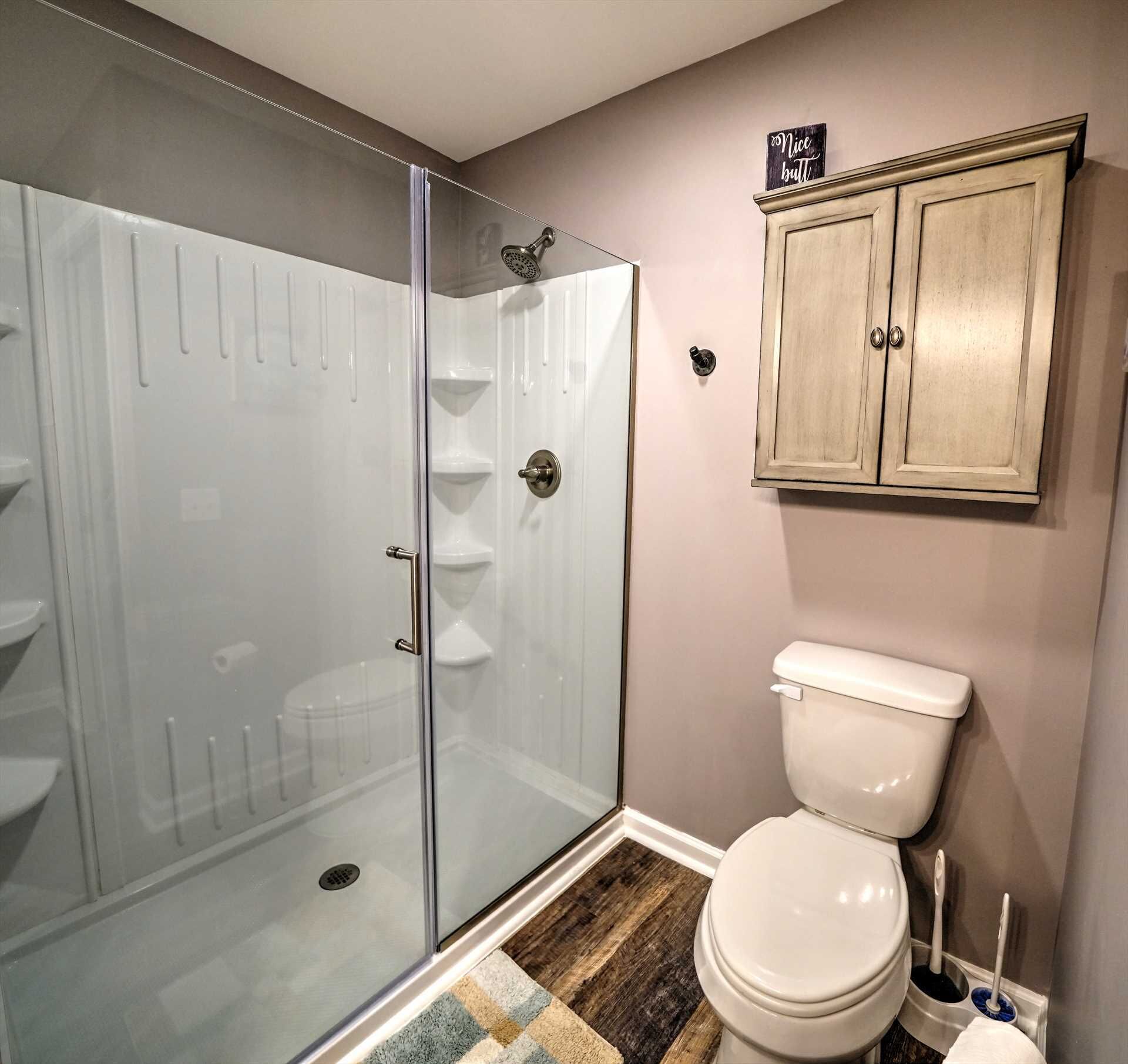 A bathroom with a glass shower enclosure, a toilet, and a wooden cabinet above the toilet.