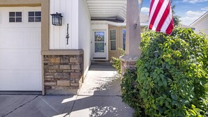A house with a white exterior, a stone foundation, a front door with a wreath, and an American flag. - Luxury 4 bed 2.5 bath home TF (Twin Falls)