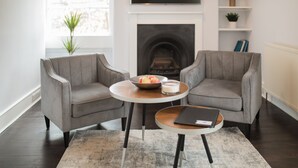 A modern living room with two grey armchairs, a round coffee table with a book, and a fireplace in the background. - River View House Cleveland Bridge (Bath)