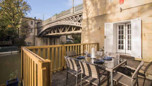 An outdoor dining area with a table set for two, overlooking a river and a bridge. - River View House Cleveland Bridge (Bath)