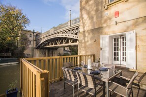 Un espace de restauration en plein air avec une table dressée pour deux personnes, offrant une vue sur une rivière et un pont.