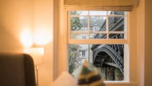 A room with a window overlooking a historic building with a metal arch bridge. - River View House Cleveland Bridge (Bath)