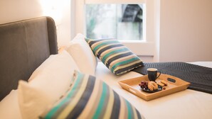 A bed with striped pillows, a tray with cookies and a cup, and a window with a view of buildings. - River View House Cleveland Bridge (Bath)