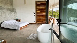 Un dormitorio moderno con una cama grande, una bañera separada y un ventanal corredero que da a un espacio exterior.