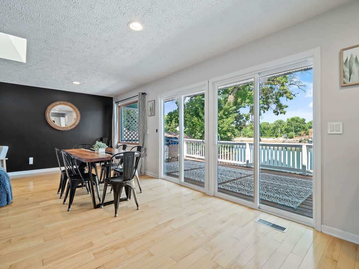 Una habitación amplia con suelo de madera, una mesa de comedor con sillas, un espejo grande y vistas a un balcón con barandilla.