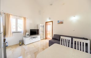 Quarto moderno com televisão de tela plana, um armário branco, sofá cinza e uma mesa de jantar.